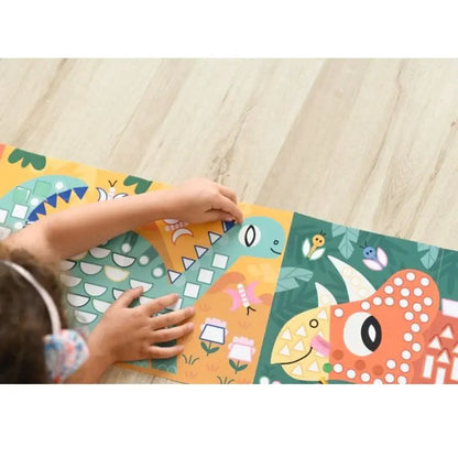 A child places sticker shapes onto the Poppik Sticker Panorama – Dinosaurs, which features a colorful green-and-yellow and a red patterned dinosaur, making it a fun and creative activity for children.