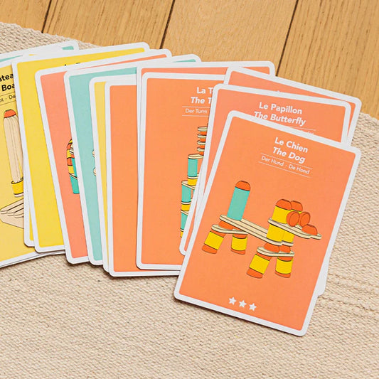 A set of bilingual Stix Construction Creative Cards flashcards with illustrations and text, laid out on a wooden surface.