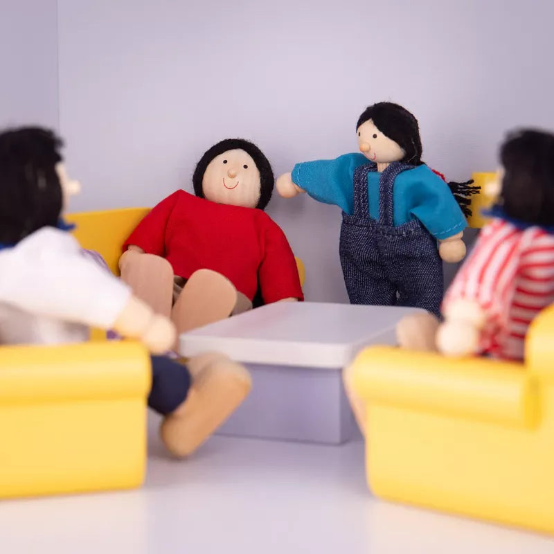 Four dolls from a Multicultural Dolls – Asian Family sit around a white table in a traditional dollhouse, staging a meeting room scene; one doll in a blue top is gesturing towards another in a red sweater.