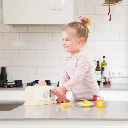 A little girl is playing with a New Classic Toys Toaster Set White in the kitchen.