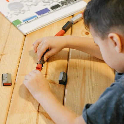 a young boy is playing with TOOBS® Figurines Trains on a wooden table.