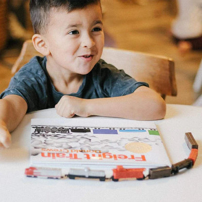 a young boy sitting at a table with TOOBS® Figurines Trains.