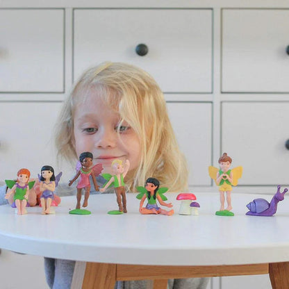 A little girl is standing in front of a table with a group of TOOBS® Figurines Friendly Fairies.