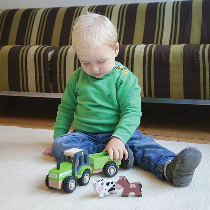 A toddler playing with a New Classic Toys Wooden Tractor with Trailer and Animals on the floor.
