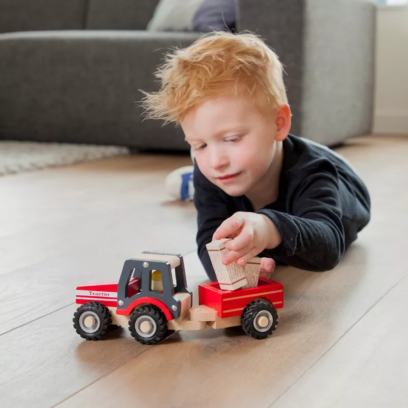 A young boy playing with the New Classic Toys Wooden Tractor with Trailer and Hay Stacks on the floor.