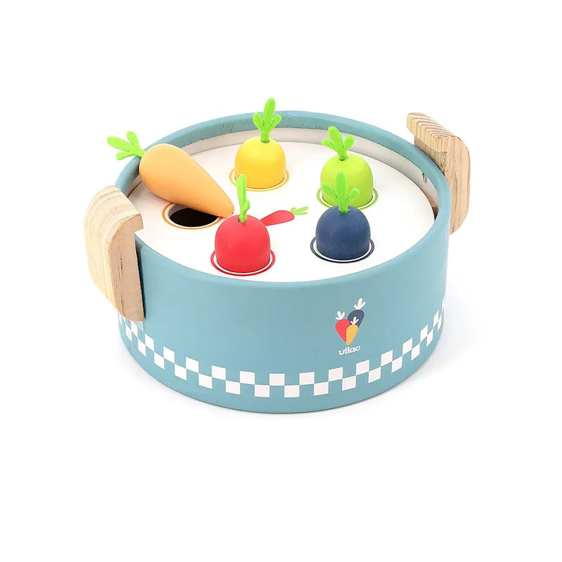 The Vilac Early Learning Cooking Pot is a charming blue wooden toy resembling a pot with two side handles and a checkered pattern around the base. Designed for toddlers 18 months and older, it contains four colorful, removable carrots (yellow, green, red, blue) with felt leaves, each fitting into corresponding slots on the lid.