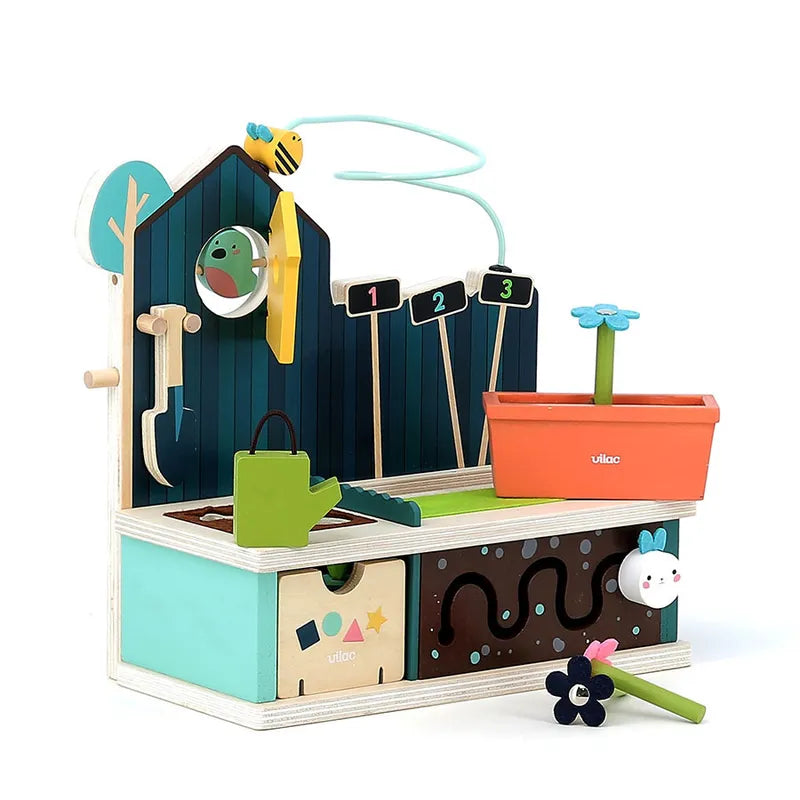 The Vilac Early Learning Garden is a vibrant wooden toy gardening set, ideal for children aged 18 months and older. This charming playset includes a shed equipped with tools, a birdhouse, a watering can, and numbered flower sticks. Completing the whimsical setting is a raised garden bed adorned with flowers and featuring an adorable worm peeking out.