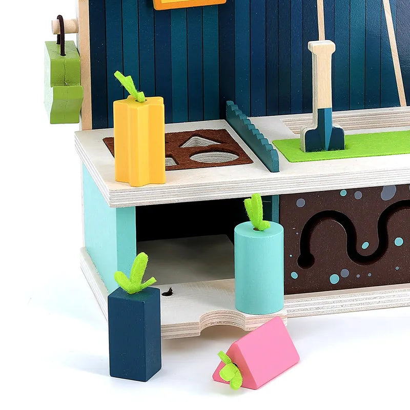 The Vilac Early Learning Garden is a vibrant wooden toy setup for children aged 18 months and older, featuring various shapes and pieces resembling a garden scene. It includes a small shovel, a green patch with a pathway, and blocky pieces topped with green felt to mimic plants. There are cut-out shapes and small compartments for added fun.