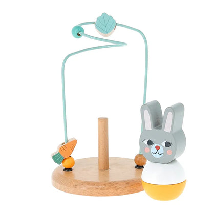 The Vilac Early Learning Game Little Rabbit is a perfect wooden toy for a 1-year-old. It features a blue squiggly wire adorned with a leaf and carrot, set on a sturdy wooden stand with a round yellow and white top that showcases a smiling gray bunny with pink cheeks.