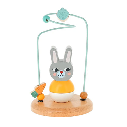 The Vilac Early Learning Game Little Rabbit is a delightful wooden toy for 1-year-olds, showcasing a grey and white bunny with rosy cheeks, perched on a round wooden base. Above the bunny are two looping green wires adorned with carrot and leaf-shaped beads, designed for sliding along the wires to provide endless play.