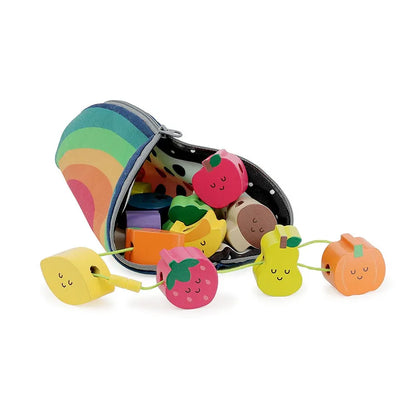 The Vilac Fruits Wooden Beads set features a colorful, rainbow-striped bag that lies open with wooden toy fruits spilling out. The toys, perfect for children aged 18 months and up, include a lemon, strawberry, pear, apple, and orange; all featuring cute faces and designed to be strung together with a green thread.