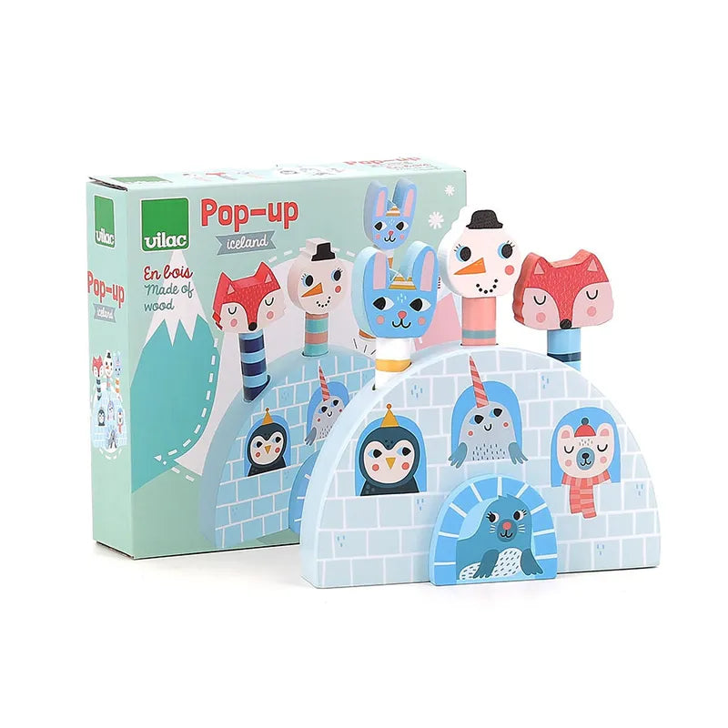 The Vilac Pop-Up Iceland toy, designed for children 18 months and older, is showcased. This wooden toy features colorful animal figures such as a penguin, fox, rabbit, and seal that pop out of an igloo backdrop. The packaging behind the toy also displays similar imagery from the Iceland collection.