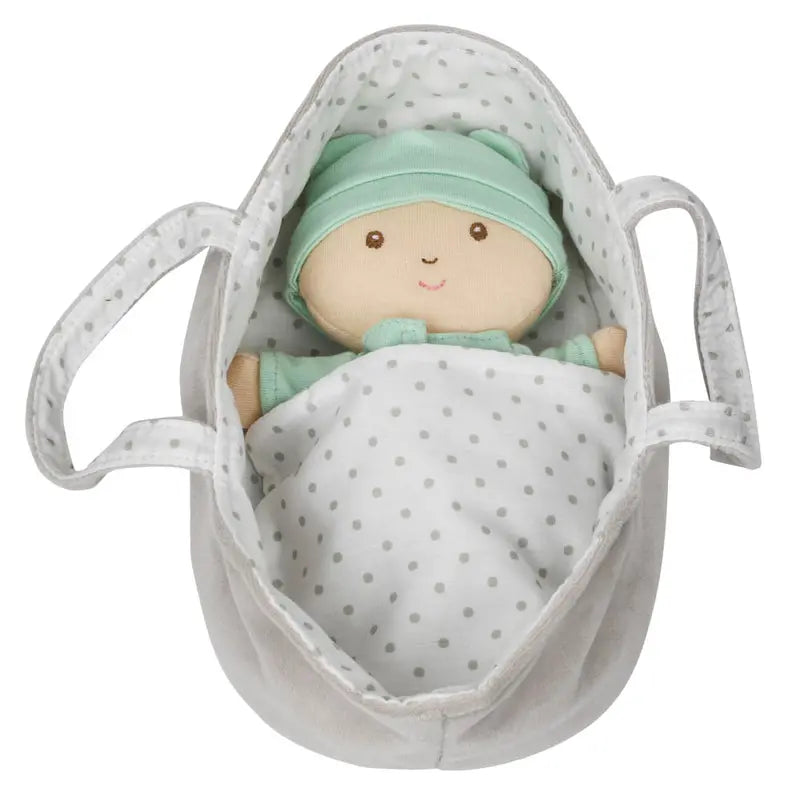The Wilberry Baby Doll in Green Outfit comes dressed in mint green clothes and hat, lying under a white polka dot blanket inside a white fabric basket with handles.