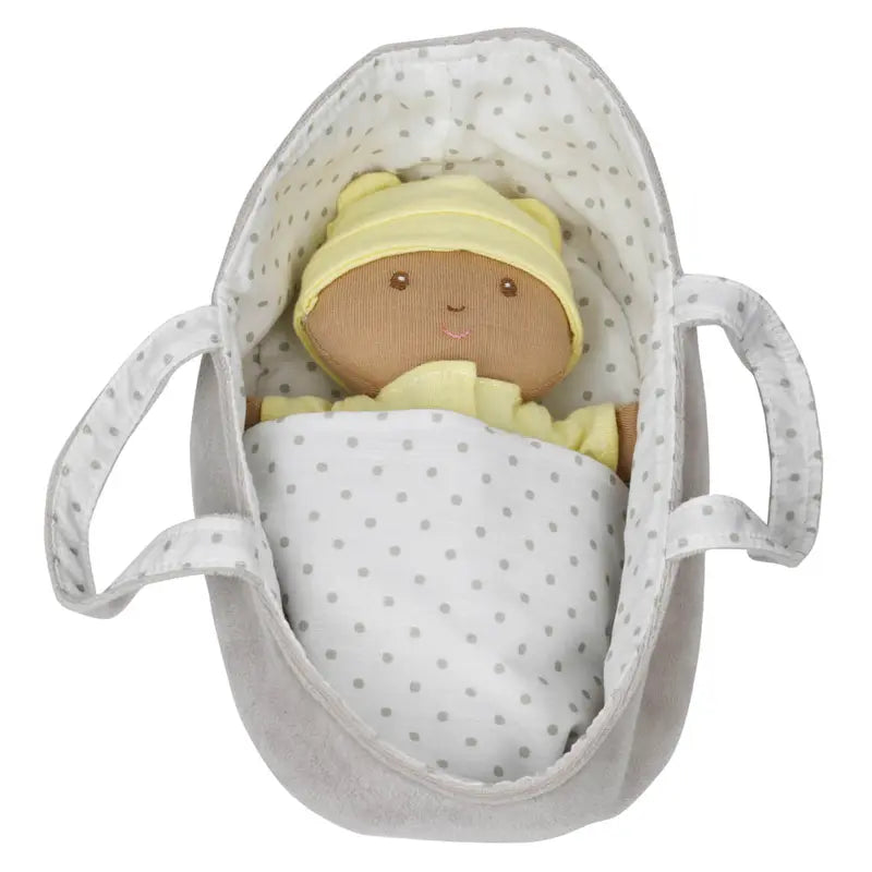 The Wilberry Baby Doll in Yellow Outfit features brown skin, a soft yellow hat and pyjamas, tucked in a white polka dot blanket inside a gray plush handled basket.