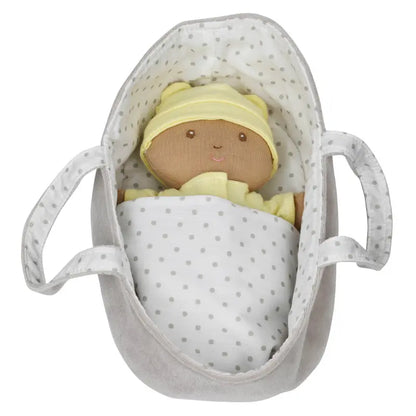 The Wilberry Baby Doll in Yellow Outfit features brown skin, a soft yellow hat and pyjamas, tucked in a white polka dot blanket inside a gray plush handled basket.
