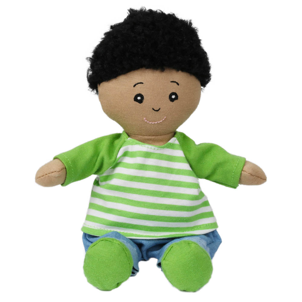 The Wilbery Baby Doll Boy Green Outfit has brown skin, curly black hair, embroidered eyes, a green-and-white striped shirt, blue pants, green booties, and sits with outstretched arms and a joyful smile.
