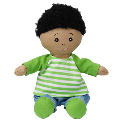 The Wilbery Baby Doll Boy Green Outfit has brown skin, curly black hair, embroidered eyes, a green-and-white striped shirt, blue pants, green booties, and sits with outstretched arms and a joyful smile.