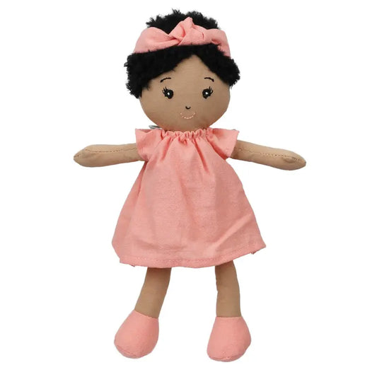 The Wilbery Baby Doll Girl Coral Outfit features a soft doll with brown skin, black curly hair, a pink headband, coral dress, and matching shoes. This smiling doll from Wilbery dolls is ready for hugs with open arms.