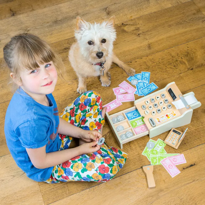 a little girl sitting on the floor next to a dog and a New Classic Toys Cash Register.