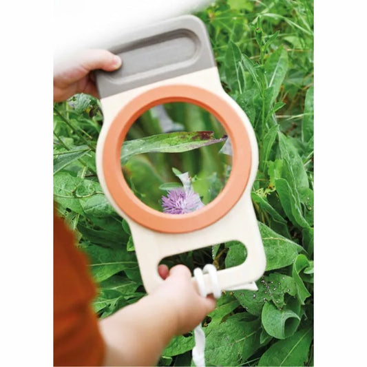 Child using a XXL Magnifying Glass “Discover” to closely observe a purple flower amidst greenery.