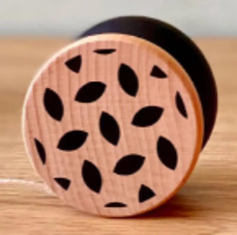 The Wooden Yo-Yo Black features a light-colored circular face with black leaf-shaped patterns and rests on a wooden surface, providing screen-free fun for all ages.