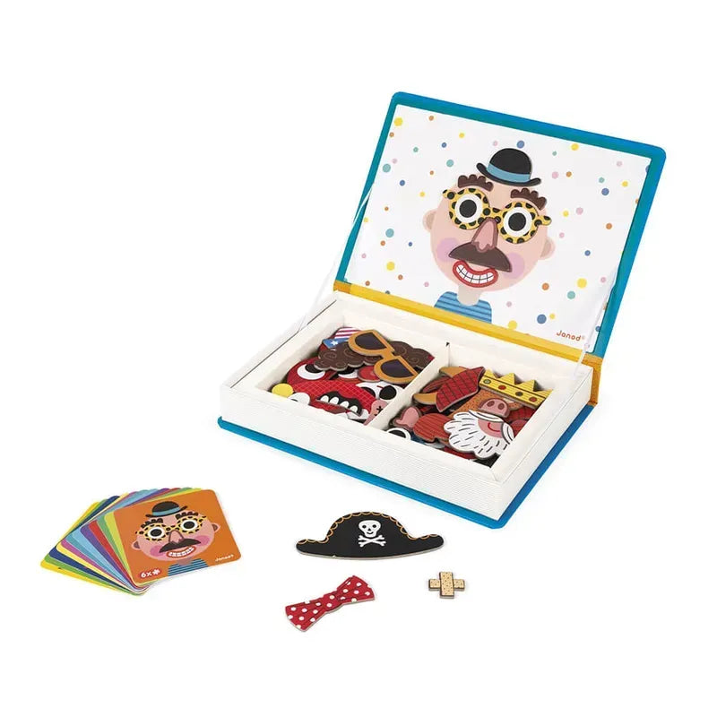 An open box contains a Janod Boy's Crazy Faces Magneti'book educational game with various magnetic facial features and accessories. Alongside the main box are several colorful cards displaying different face designs. Some accessories, including a pirate hat and bow tie, are spread out.