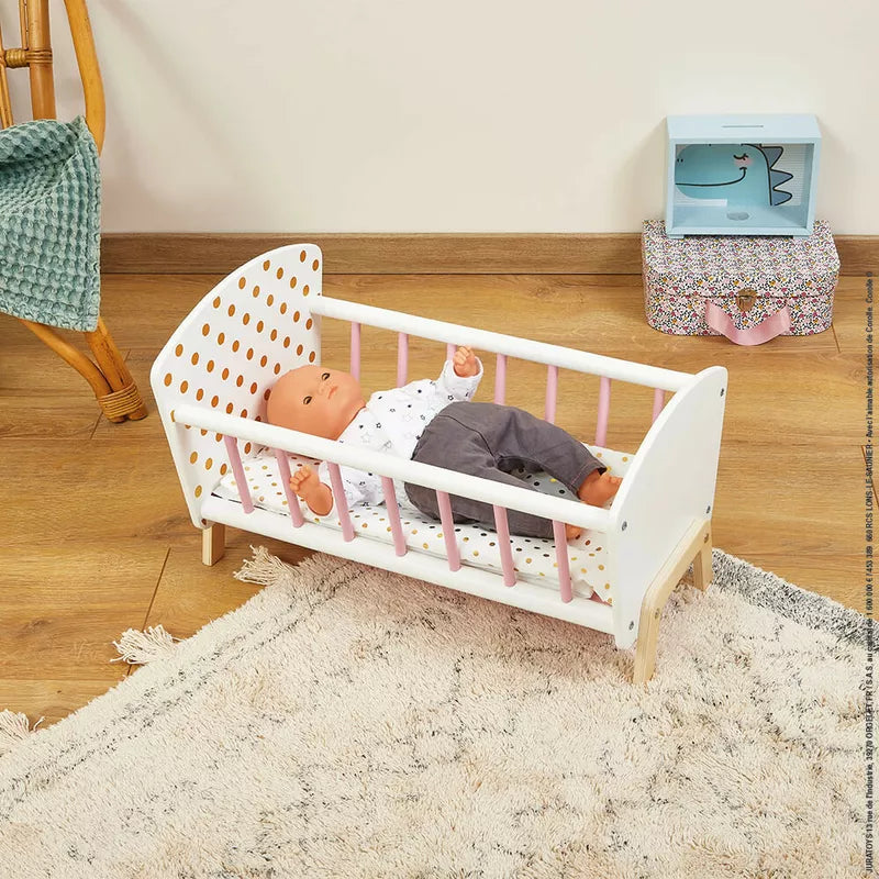 A Janod Candy Chic Doll's Bed holding a baby doll on the floor.