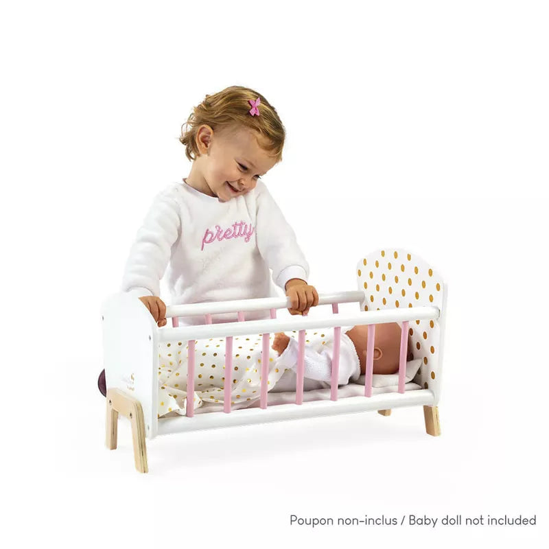 A baby girl smiling while holding the Janod Candy Chic Doll's Bed.