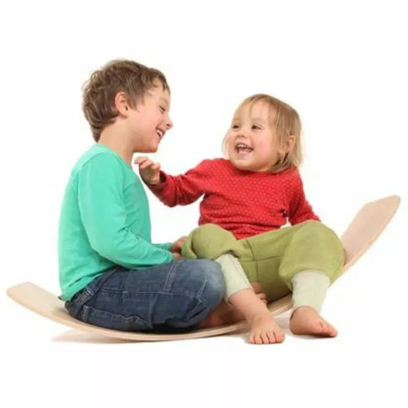 Two young children, a boy and a girl, are joyfully sitting on a das.Brett Bouncy Wooden Balance Board Lacquered with Cork Bottom-side Cladding, laughing and playing together against a white background.