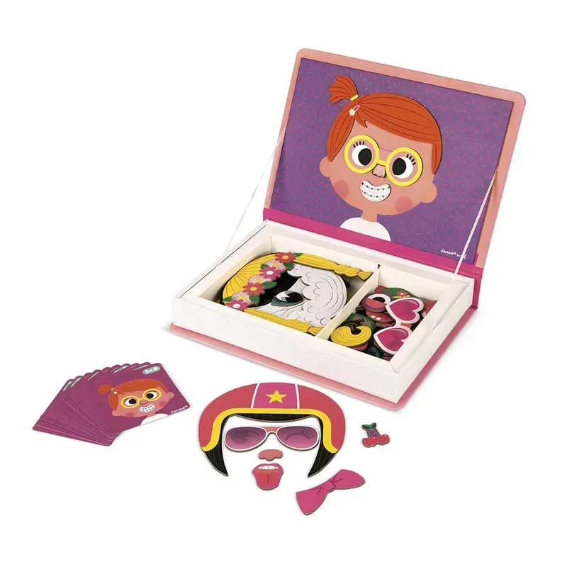 A children's Janod Girl's Crazy Faces Magneti'book set is displayed. This educational magnetic game includes a booklet with a picture of a girl and various magnetic face parts such as eyes, glasses, hair, and accessories. Additional magnetic pieces and cards are spread out beside the booklet.