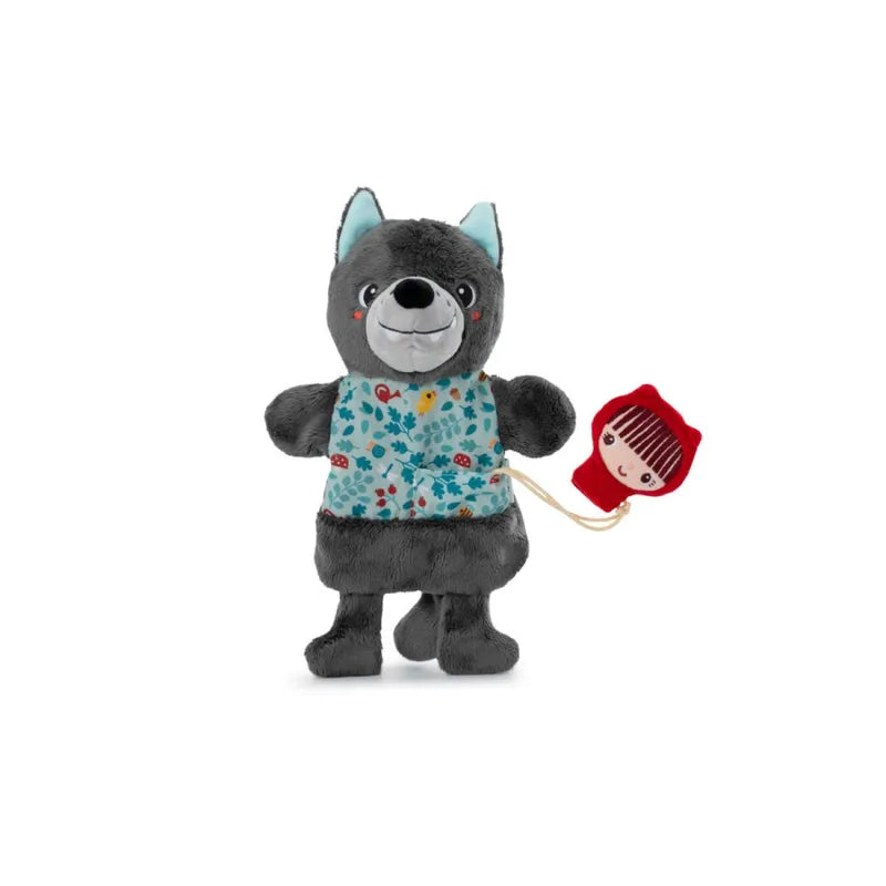 A gray stuffed wolf toy with blue ears is wearing a teal and red floral vest. It holds a small Little Red Riding Hood Finger Puppet by a string in its left paw. The Lilliputiens Louis Wolf Handpuppet, designed for imaginative and creative play, has a joyful expression with a wide smile.