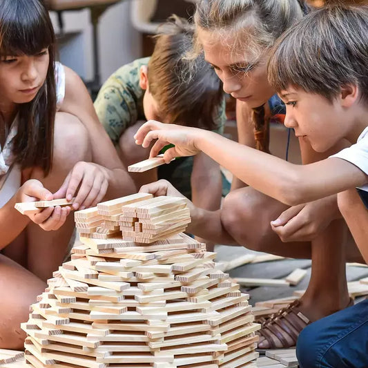 Children engaged in a careful game with KAPLA® Construction 1000 Planks in Wooden Box, concentrating intensely on placing each piece without causing a collapse.