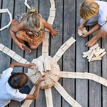 Three children engaged in creativity toys, building an intricate network of wooden tracks with KAPLA® Construction 1000 Planks in Wooden Box on a wooden deck floor.