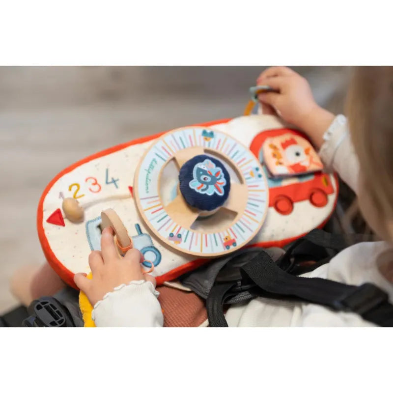 A child playing with a colorful Lilliputiens Farm Car Activity Panel. This Lilliputiens Farm Car Activity Panel features a steering wheel, illustrated characters, numbers, and other interactive elements. The child is engaged and interacting with the car activity toy, designed for learning and development.