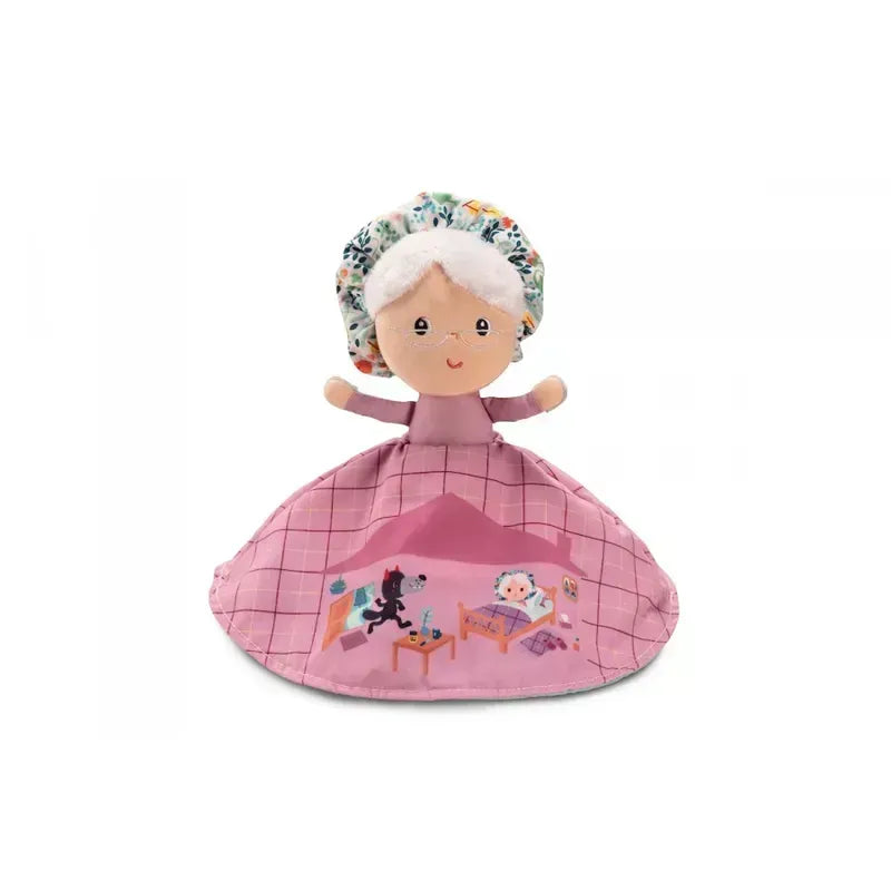 The Lilliputiens Little Red Riding Hood Reversible Storydoll is a charming fabric doll with white hair, dressed in a floral bonnet and a pink dress. The dress showcases a printed scene of a small dog interacting with a table and chair. The smiling face has stitched eyes and mouth, making it ideal for both storytelling play and use as a reversible hand puppet for Little Red Riding Hood tales.