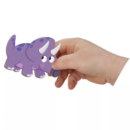 A hand holding a Janod Magneti'stories Dinosaurs magnetic game piece against a white background.