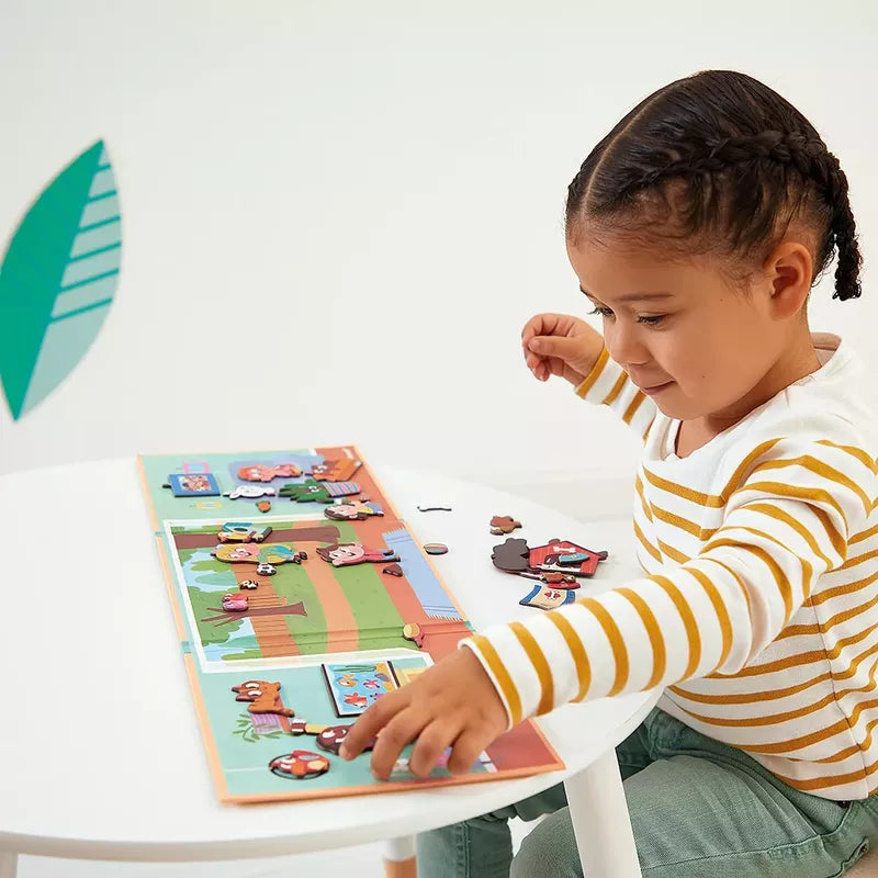 A young child is focused and enjoying a Janod Magneti'stories Pets game on a white table, with pieces scattered around depicting pets-themed magnets and scenes.