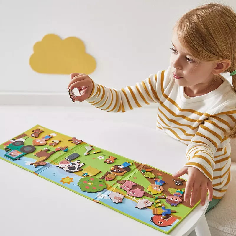 A young child engaging in a puzzle-solving activity, carefully placing a piece on a Janod Magneti'stories The Farm magnetic game board.