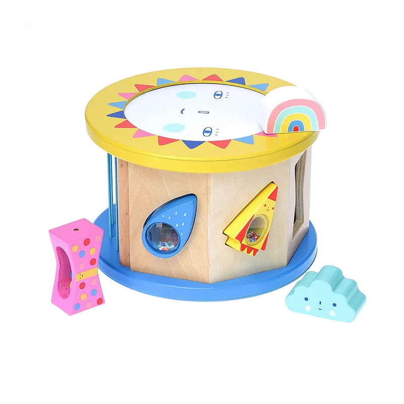 Introducing the Vilac Night and Day Shape Sorter: a charming round wooden baby toy featuring colorful geometric shapes and a rotating sun design on top. This shape sorter includes cutouts for three distinct shapes—a pink block, a yellow and red block, and a blue cloud shape. Additionally, it features a small rainbow decoration perched on top to enhance fine motor skills.