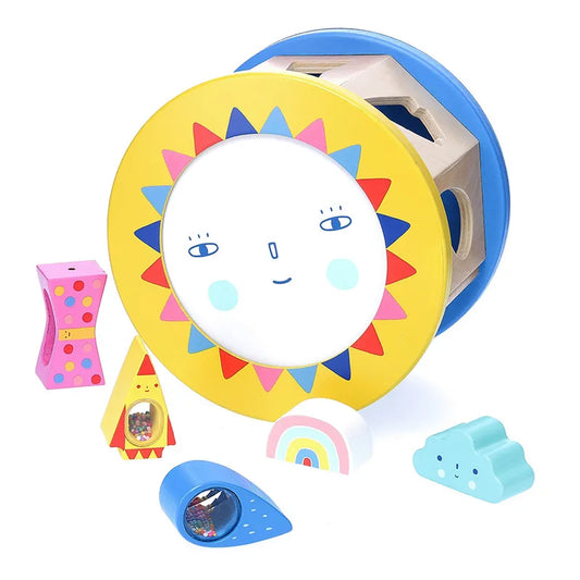 The Vilac Night and Day Shape Sorter is a vibrant wooden baby toy featuring a yellow sun-like circular frame with a face. It comes with shape pieces including a pink flower, chicken, cloud, rainbow, and blue raindrop—some of which are filled with tiny beads—all designed to help develop fine motor skills.