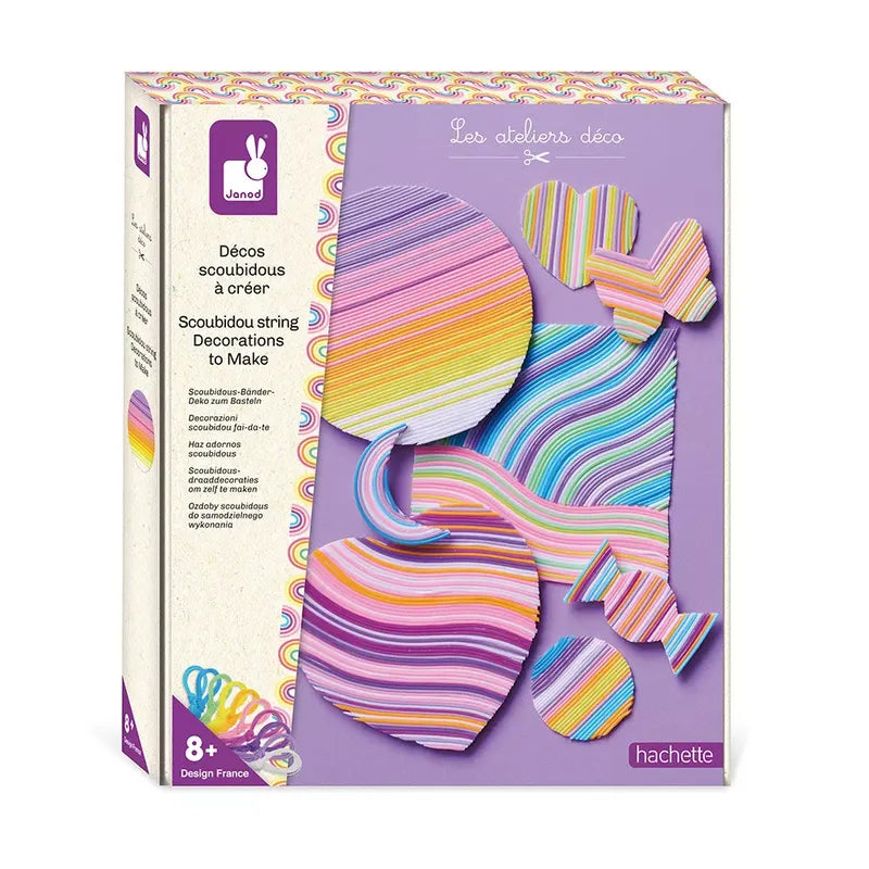 The image shows a craft kit from Janod, titled "Janod Scoobies String Decorations To Make." The packaging is purple and features colorful string art shapes like hearts and circles. This creative activity is perfect as a birthday gift for 8-year-old artists, as it is recommended for ages 8 and up.