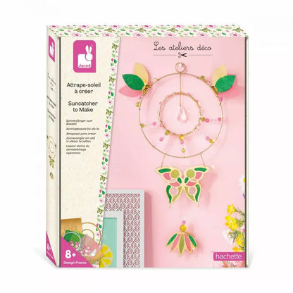 Box of the Janod Suncatcher To Make kit for kids. The box displays an illustration of the finished sun catcher, featuring a circular frame adorned with leaves, a butterfly, and a hanging gem. Text on the box includes product details and the brand, Janod, along with age recommendation (8+). This delightful children's craft kit doubles as a decorative toy.