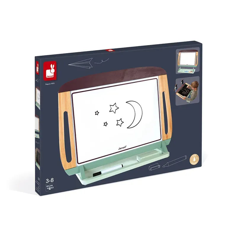 A product box featuring the Janod White and Blackboard Table, which includes a double-sided blackboard and whiteboard with built-in storage and two wooden handles. The board surface displays drawings of stars and a crescent moon, and the box features an illustration of a child using the board to highlight its magnetic whiteboard feature. Suitable for ages 3-8.