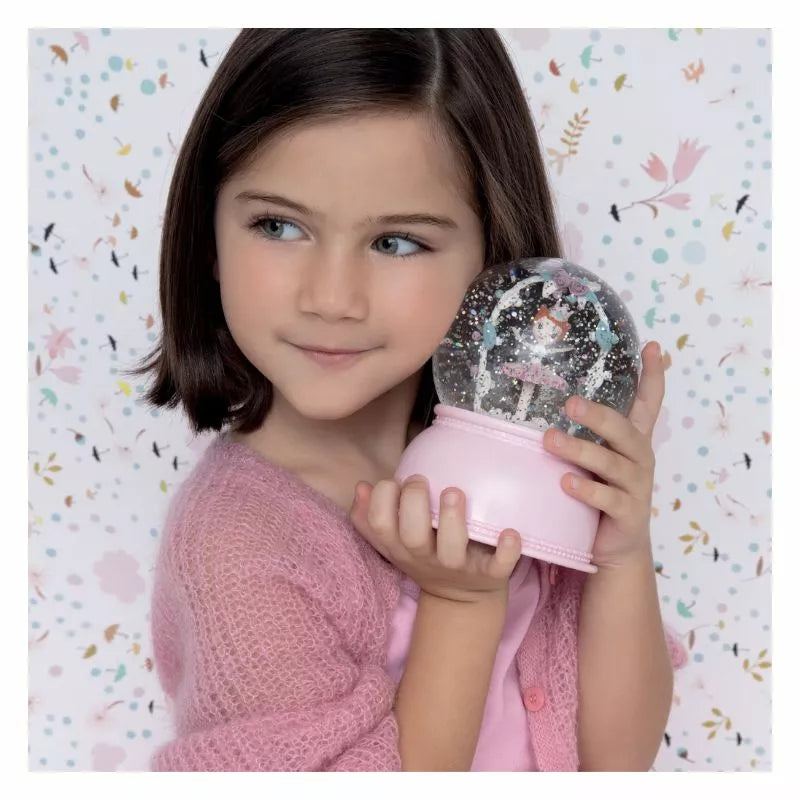 A little girl holding a Djeco Snow Ball Nightlight Ballerina in her hand.