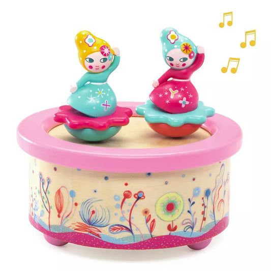 A Djeco Musical Box Flower Melody with two dolls sitting on top of it.