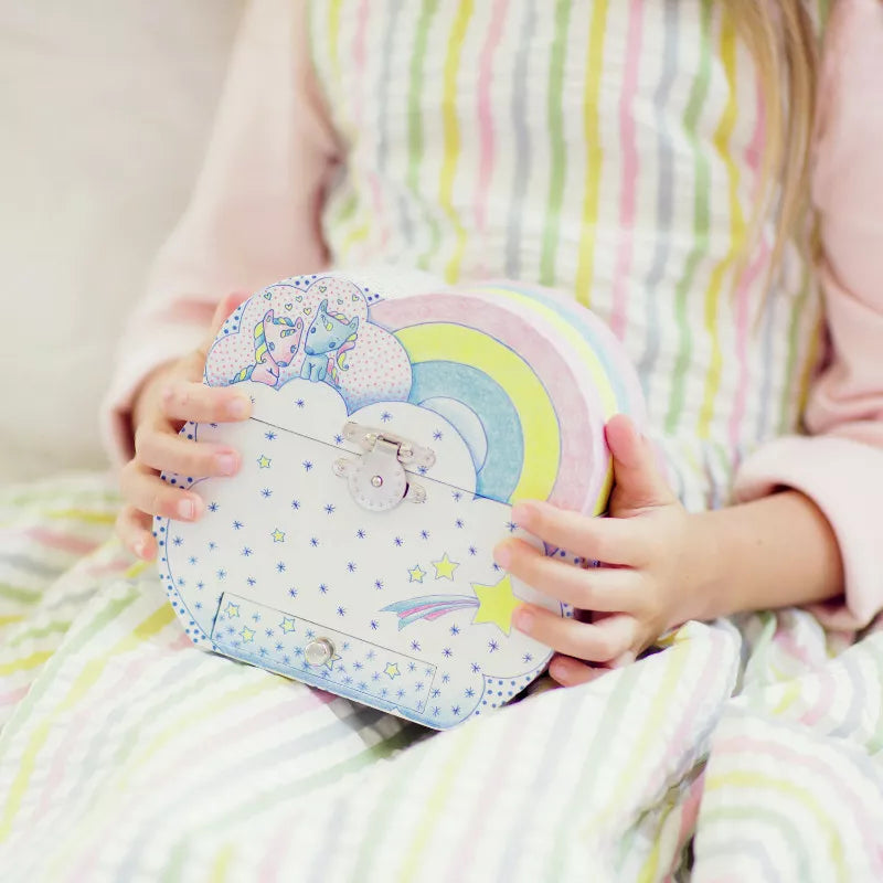 A little girl sitting on a bed holding a Djeco Musical Box Dreams of unicorn.